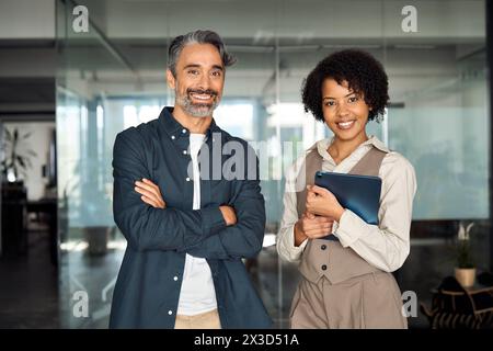 Zwei verschiedene Geschäftspartner stehen im Büro und schauen auf Kamera und Porträt. Stockfoto