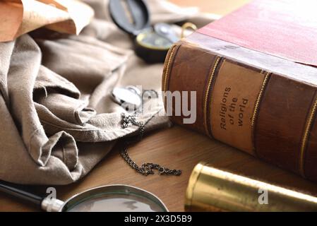 Altes und verschlechtertes Buch der Religionen der Welt mit alten Studien- und Abenteuergegenständen auf Holztisch. Erhöhte Aussicht. Stockfoto