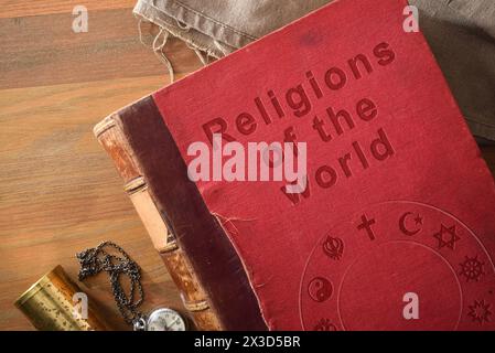 Detail des alten Buches über das Studium der Religionen in der Welt mit graviertem Text und Symbolen verschiedener Religionen auf Holztisch mit dekorativen Objekten. Stockfoto