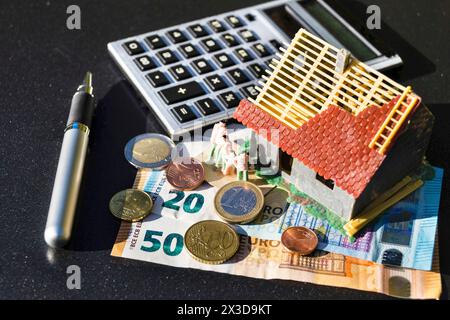 Unvollendetes Modellhaus, Taschenrechner, Stift und Geld symbolisieren den Anstieg der Immobilienpreise Stockfoto