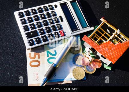 Unvollendetes Modellhaus, Taschenrechner, Stift und Geld symbolisieren den Anstieg der Immobilienpreise Stockfoto