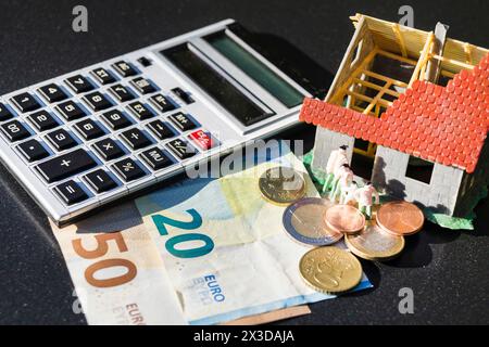 Unvollendetes Modellhaus, Taschenrechner, Stift und Geld symbolisieren den Anstieg der Immobilienpreise Stockfoto