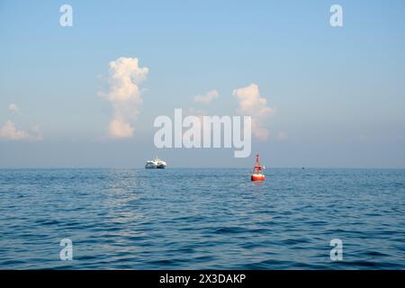 Ein einsames Boot treibt auf dem ruhigen Meer, unter dem wachsamen Blick der flauschigen Wolken, in einem Tanz der Natur und der menschlichen Gegenwart. Stockfoto