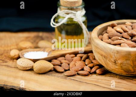 Mandel (Prunus dulcis, Prunus amygdalus, Amygdalus communis, Amygdalus dulcis), gesalzene Mandeln in einer Holzschale mit ungesackten Mandeln, Löffel mit sal Stockfoto
