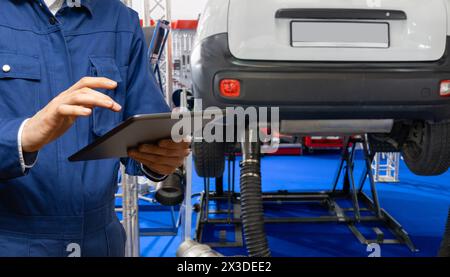 Servicemitarbeiter mit digitalem Tablet auf dem Hintergrund des Fahrzeugs im Autoservice Stockfoto