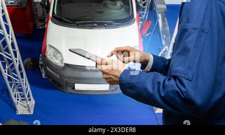 Servicemitarbeiter mit digitalem Tablet auf dem Hintergrund des Fahrzeugs im Autoservice Stockfoto