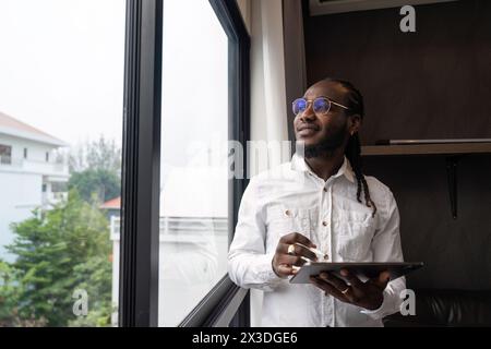 Glücklicher afrikanischer Mann, der ein Tablet im Wohnzimmer benutzt Stockfoto
