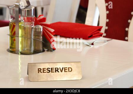 Reservierte Metallplatte mit Aufschrift: Reserviert auf einem arrangierten weißen Tisch im Restaurant Stockfoto