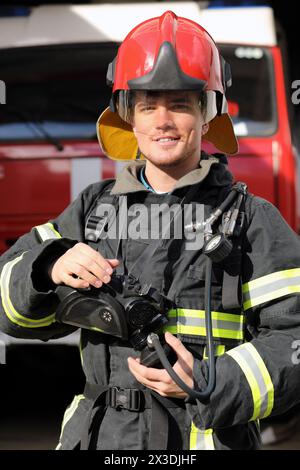 Porträt eines lächelnden Feuerwehrmannes mit Feuerwehrkugeln und rotem Helm Stockfoto