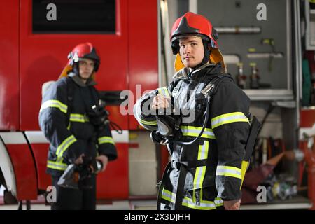 Zwei Feuerwehrleute in Schutzkleidung, Helmen und Maske gegen Feuerwehrauto Stockfoto