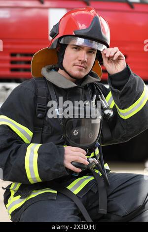 Porträt des Feuerwehrmannes mit Feuerwehrkugeln und rotem Helm, Hand auf Visier Stockfoto