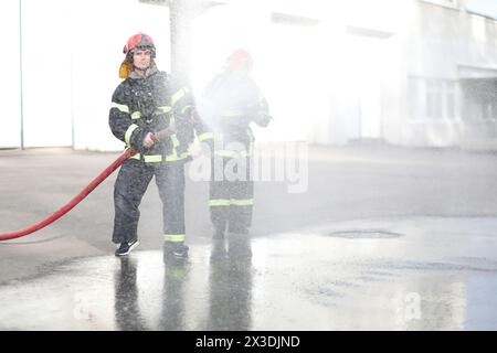 Porträt von zwei Feuerwehrmännern hält und passt Düse und Feuerwehrschlauch an, die Hochdruckwasser sprühen Stockfoto