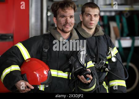 Zwei Feuerwehrmänner in Schutzanzügen, die gegen Feuerwehrfahrzeuge stehen Stockfoto