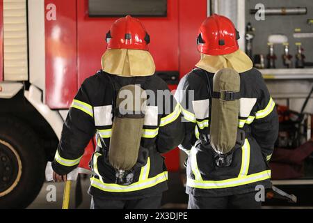 Zwei Feuerwehrleute in Ausrüstung und Helme gegen Feuerwehrauto, Rückansicht Stockfoto