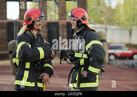 Zwei Feuerwehrleute in Ausrüstung und Helmen auf der Teststelle, kommunizieren, lächeln Stockfoto