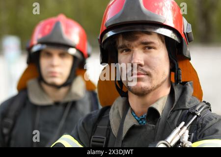 Porträt von zwei heldenhaften Feuerwehrleuten in Schutzanzug und rotem Helm, Nahaufnahme Stockfoto