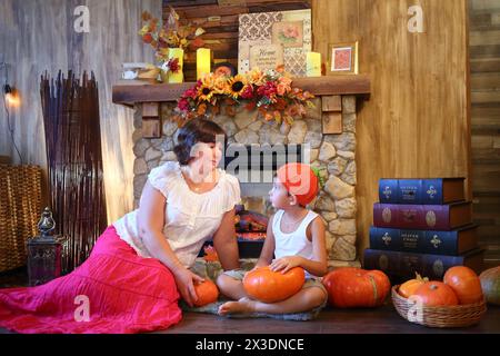 Mutter und Sohn in orangefarbener Mütze mit Kürbissen sitzen vor einem Kamin Stockfoto