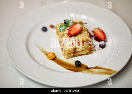 Den Kuchen mit Minze, Erdbeere, Heidelbeere und Sauce auf den Teller legen. Stockfoto