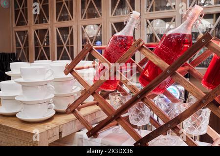 Flaschen mit rotem Getränk, Weingläser und Tassen auf Holztisch. Stockfoto
