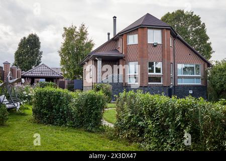 Modernes Landhaus aus rotem Backstein und Garten mit Blumen, Büschen, Bäumen. Stockfoto
