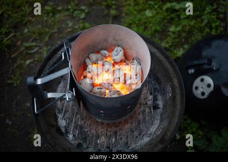 Grill im Freien mit brennenden Holzkohlen und Metalltopf mit in Folie gebackener Kartoffel. Stockfoto