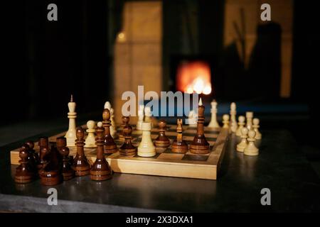 Schachbrett mit Schachfiguren in dunklem Raum mit Kamin im Hintergrund. Stockfoto