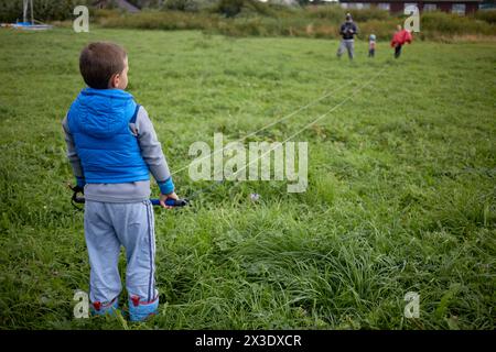 Boy steht mit einer Steuerstange mit angebrachten fliegenden Linien von Power-Kite auf grüner Wiese, Blick von hinten. Stockfoto