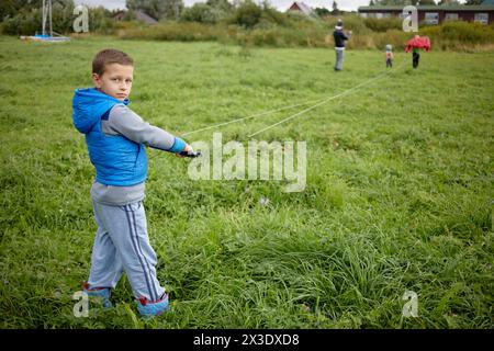 Junge steht mit einer Steuerstange und angebrachten Drahtseilen auf grüner Wiese, Blick von hinten. Stockfoto