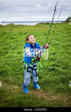 Junge, der für Kitesurfen ausgerüstet ist, lernt, Power-Kite auf grüner Wiese zu steuern. Stockfoto