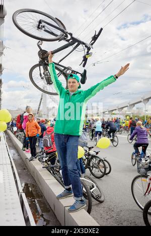 Der Vater steht mit dem Fahrrad in einer Hand hoch über dem Kopf gegen die Tochter und die Menschenmenge auf und mit den Fahrrädern auf der Straße Stockfoto