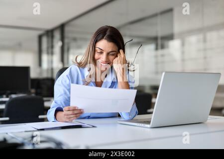 Glückliche, beschäftigte Geschäftsfrau mittleren Alters, die im Büro arbeitet und Dokumente liest. Stockfoto
