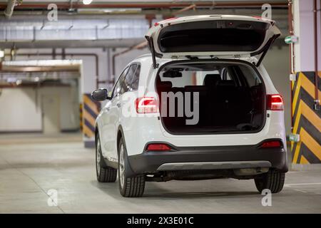 Modernes weißes Auto mit offener Kofferraumtür in der Tiefgarage. Stockfoto