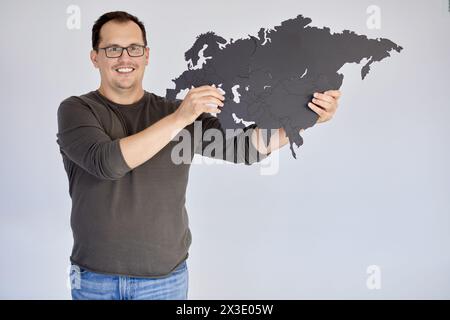 Ein lächelnder Mann in Brille hält eine Puzzlekarte von Eurasien. Stockfoto