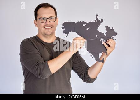 Ein lächelnder Mann in Brille hält eine Puzzlekarte Nordamerikas. Stockfoto