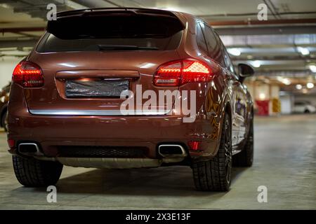 Neues modernes Auto mit eingeschalteten Rückleuchten in der Tiefgarage, Ansicht von hinten rechts. Stockfoto