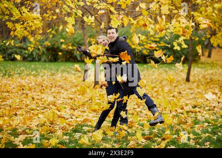 Mann und Frau spielen im Herbstpark und werfen gefallene Blätter hoch. Stockfoto