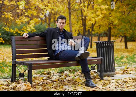 Der Mann sitzt auf einer Bank im Herbstpark und raucht Zigarren. Stockfoto