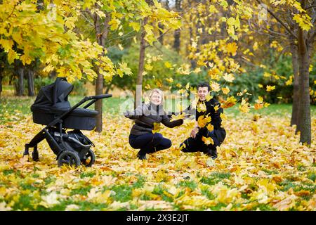 Mann und Frau sitzen unter fallenden gelben Blättern in der Nähe von Pambulator im Herbstpark. Stockfoto