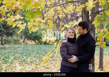 Mann und Frau stehen umarmt unter Ahornbaum im Herbstpark. Stockfoto