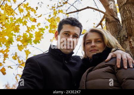 Porträt eines lächelnden Mannes und einer Frau, die am Herbsttag unter einem Ahornbaum stehen. Stockfoto