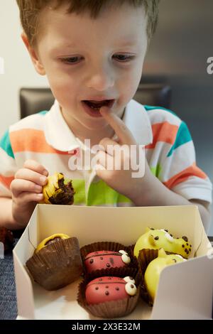 Kleiner Junge im gestreiften Polokragen isst Kuchen am Tisch. Stockfoto