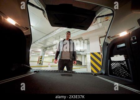 Der Mann schließt die Kofferraumtür des Autos in der Tiefgarage. Stockfoto
