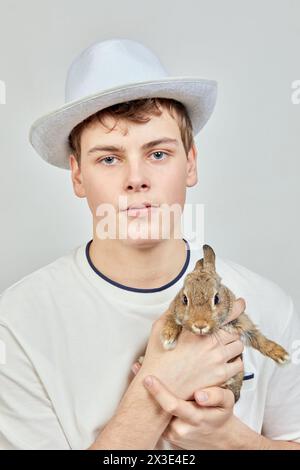 Porträt eines Jungen mit Hut, der Kaninchen in Waffen hält. Stockfoto