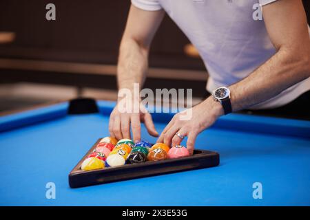 Der Mann bereitet Bälle auf einem blauen Billardtisch vor und richtet sie in einem Dreiecksregal aus. Stockfoto