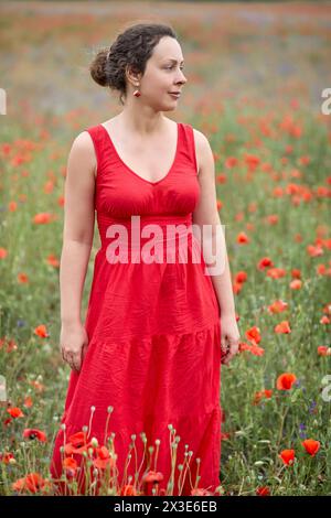 Frau in rotem Kleid steht auf rotem Mohnfeld. Stockfoto