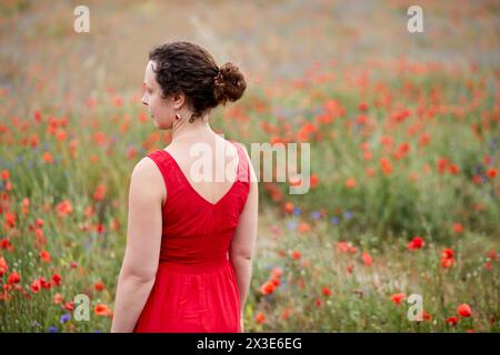 Frau in rotem Kleid steht auf blühendem rotem Mohn. Stockfoto