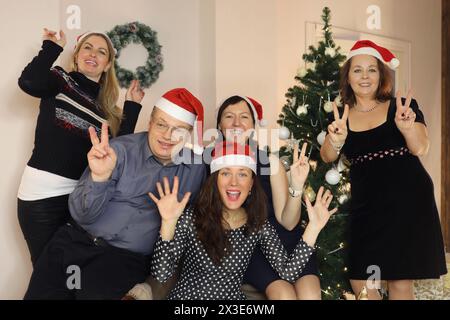 Fünf Menschen in santa Caps posieren in der Nähe des weihnachtsbaums, konzentrieren sich auf Mann und Frau in der Mitte Stockfoto