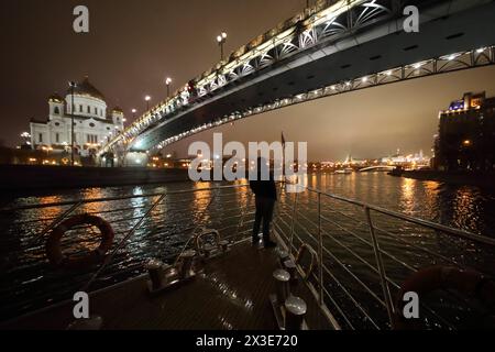 Der Mann segelt auf einem Schiff in Moskau unter der Patriarchalbrücke in der Nähe der Kathedrale Christi Erlöser bei Nacht Stockfoto