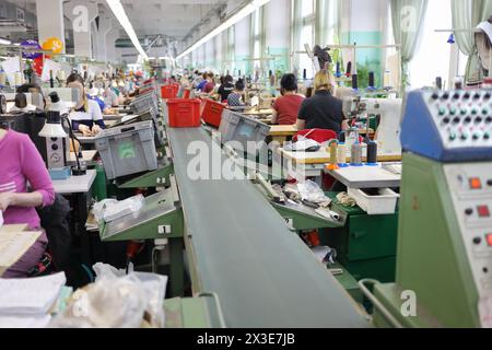 Arbeiter in der Nähe der Montagelinie in einer großen Werkstatt moderner Schuhfabrik Stockfoto