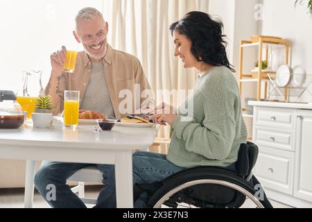 Ein Mann und eine Frau im Rollstuhl, die zusammen in ihrer Küche frühstücken. Stockfoto